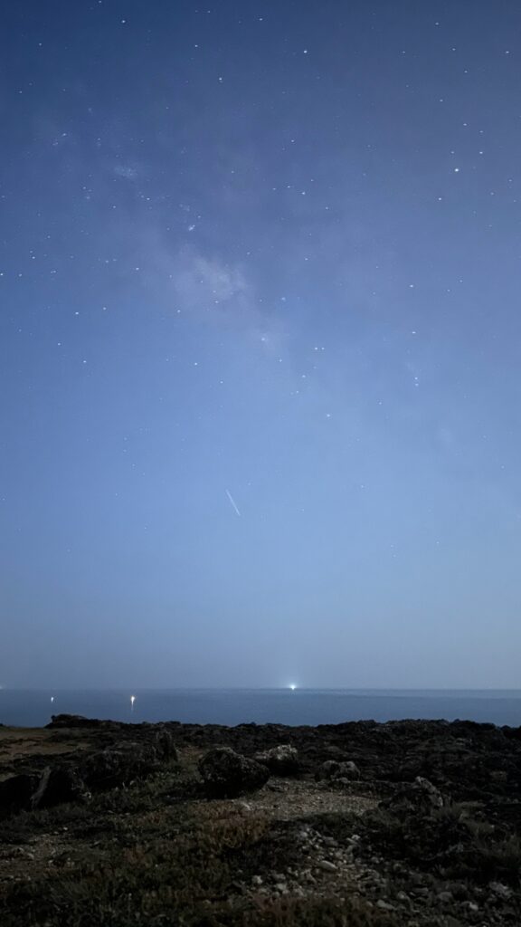 夜空布滿星點，下方是海平線上的幾點船燈與礁岩地面