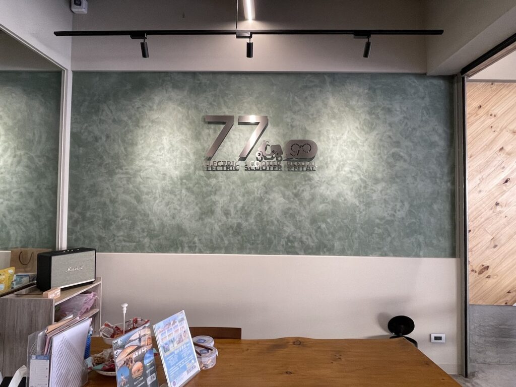77go 門市內的木質櫃檯,後方綠色牆面掛著 77go 立體招牌