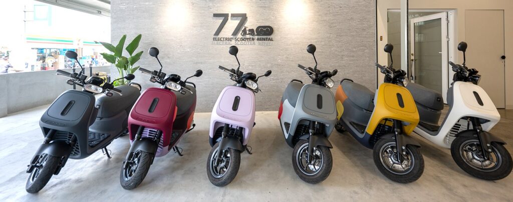 六台不同顏色的 gogoro 電動機車在 77go 門市內排成一列，後方牆上是 77go 招牌