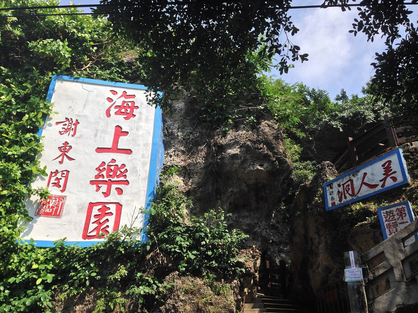 美人洞入口，珊瑚礁岩上掛著海上樂園與美人洞的紅字看板