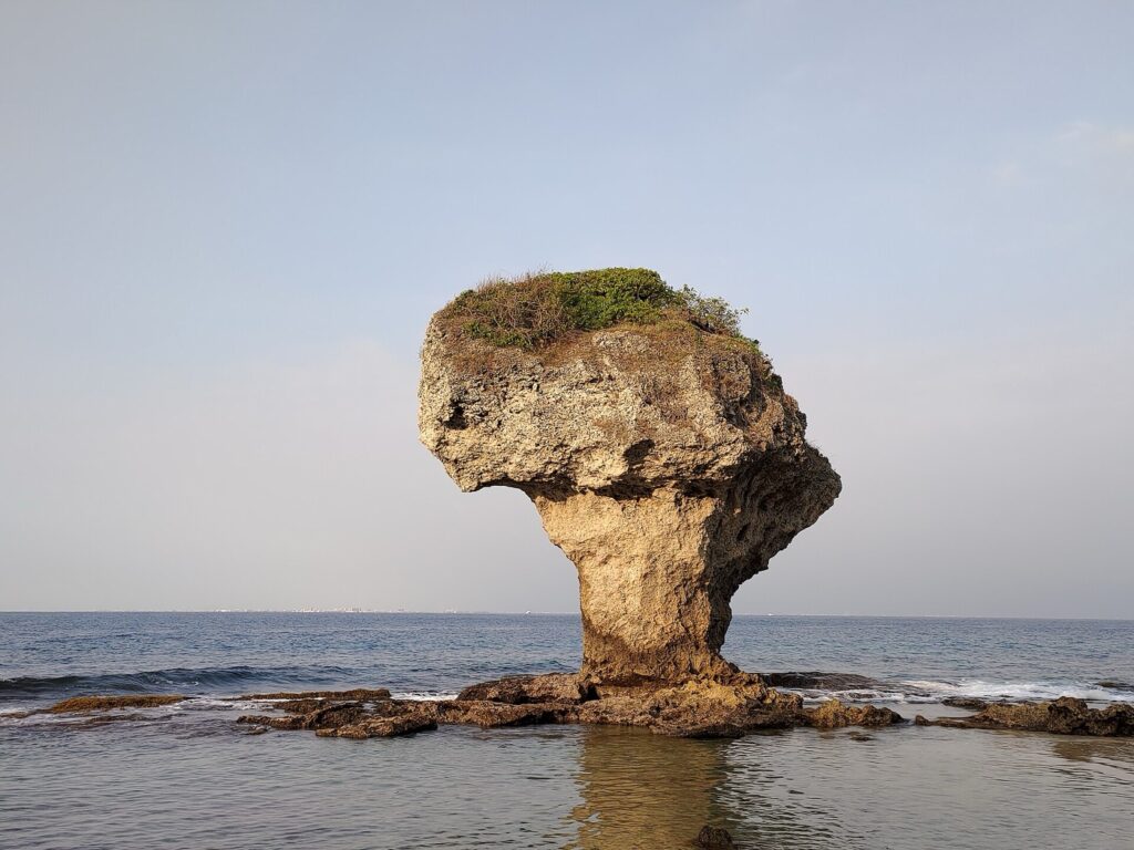 斜射光下的花瓶岩立在平靜海面上,遠景是台灣本島海岸線